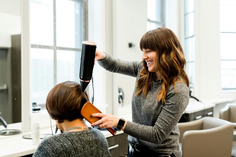 Une coiffeuse souriante coiffe une cliente dans son salon
